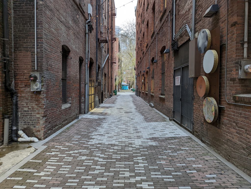 Facing north, a picture of North Alley in Pioneer Square. There is public art mounted on to one of the buildings. 