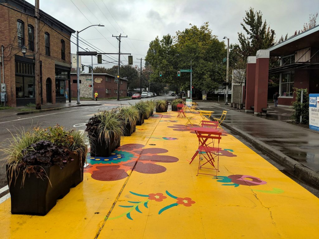 A photo of a colorfully painted parklet on a street in front of a public library. 