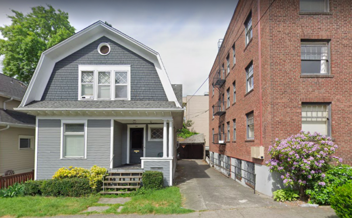 A photo of a single family dwelling and an apartment building separated by an alley.