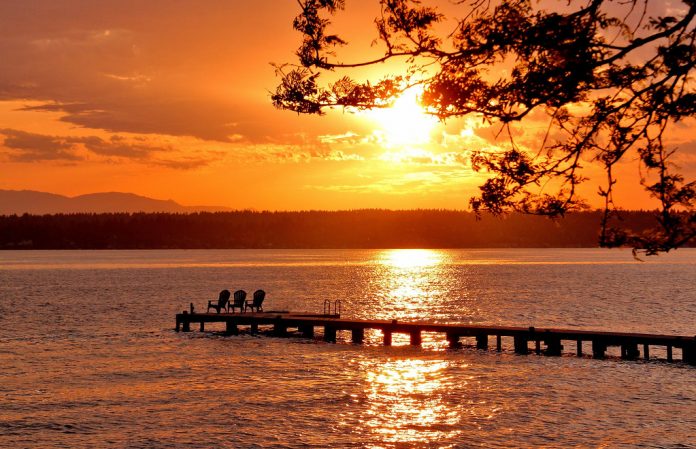A view of a sunset over a lake with a pier in it.