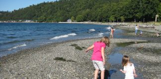 A photo of two young children on a beach with more children visible in the distance.