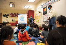 What Seattle Public Schools Needs to Say Right Now Children sit in a classroom and listen to a story being read aloud by a man in a suit wearing a mask.