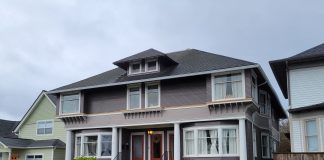 A photo of a grey triplex with red doors that maintains the scale of a large single family house.