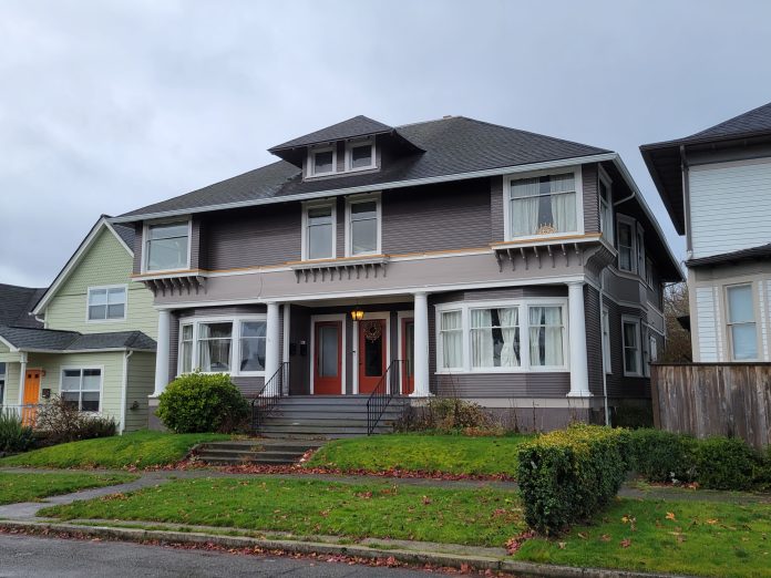 A photo of a grey triplex with red doors that maintains the scale of a large single family house.