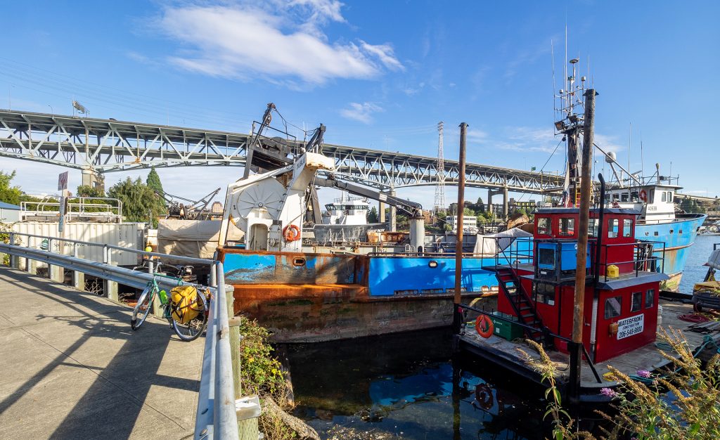 A photo of boats in the water next to a bike path with a bike parked on it.