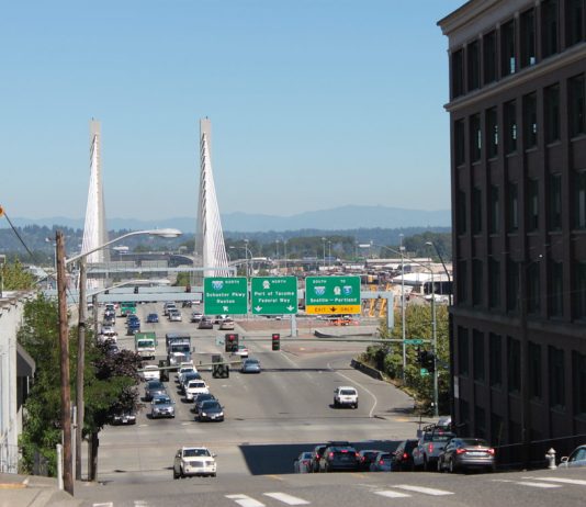 Tacoma Seeks Input for Vision Zero Safe Streets Action Plan A photo of an crosswalk on a wide street with street signs and a bridge in the distance.