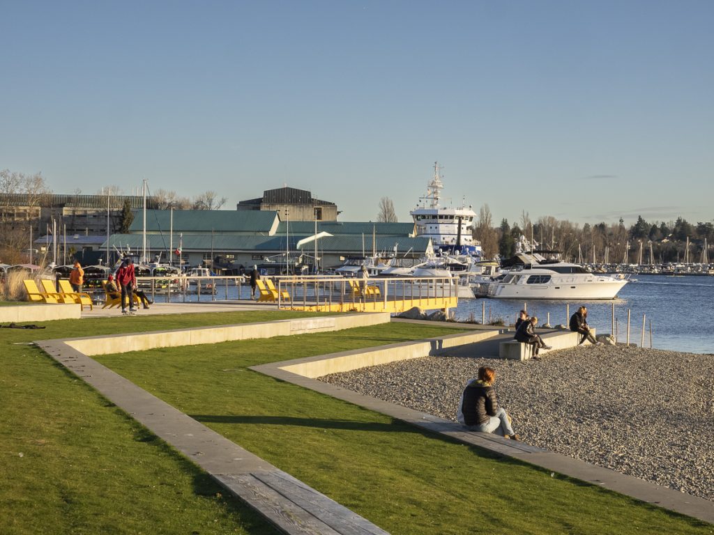 A photo of a park next to the water with grassy steps and a beach. 