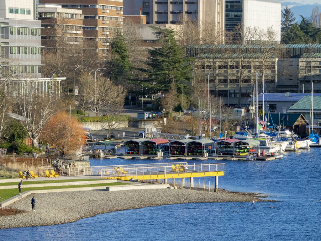 A photo of a pier with chairs over looking a lake with boats in the background. 