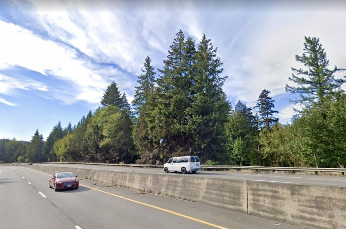 A view of a highway with two cars driving in opposite directions divided by a concrete barrier.