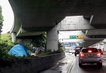 Inslee Pushes Legislation Prioritizing Homeless Encampment Removal Near Highways a photo of a freeway with cars and a tent behind a concrete barrier.