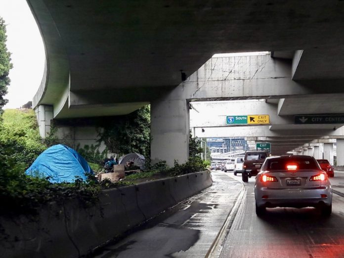 a photo of a freeway with cars and a tent behind a concrete barrier.