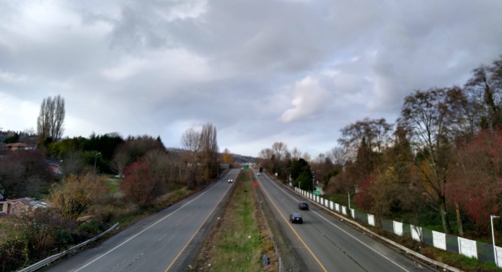 A four lane highway with a grassy median, neighborhood on either side