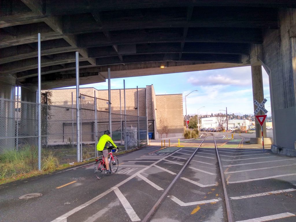 Cyclist in high viz bikes toward infrastructure directing them to cross railroad tracks at a right angle