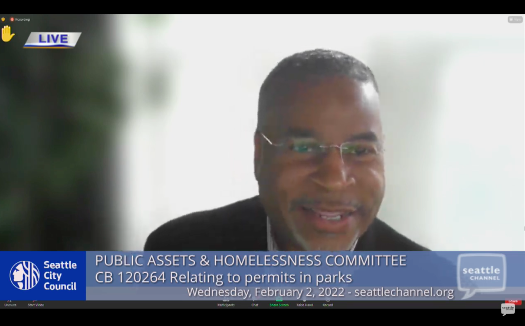 A screen shot of a smiling man wearing glasses speaking a Seattle City Council online meeting. 