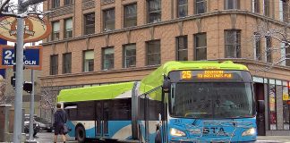 An articulated Route 25 bus in Spokane makes a turn on a downtown street after yielding to a passing pedestrian.