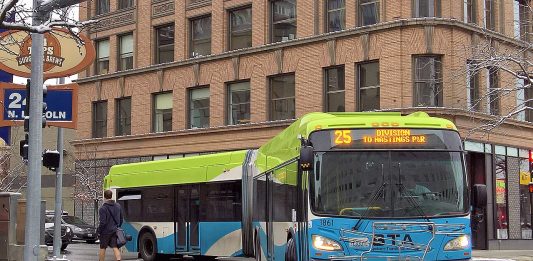 An articulated Route 25 bus in Spokane makes a turn on a downtown street after yielding to a passing pedestrian.