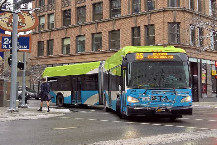 An articulated Route 25 bus in Spokane makes a turn on a downtown street after yielding to a passing pedestrian.