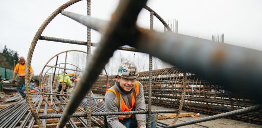 An ironworker stands inside a big rebar column and smiles for the camera.