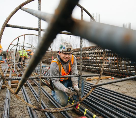 Concrete Could Flow for West Seattle Bridge and Light Rail Projects as Teamsters Offer to Return to Work An ironworker stands inside a big rebar column and smiles for the camera.