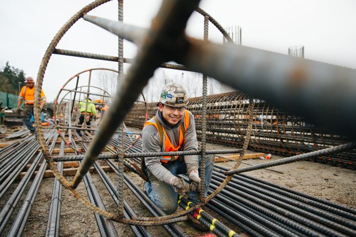 25940326137_673ef52cdc_k An ironworker stands inside a big rebar column and smiles for the camera.