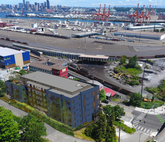 Housing Notes: 16-Story Tower Proposed in Kirkland and 114 Middle-Income Homes in West Seattle A photo of West Seattle near the bridge and Harbor Island with a rendering of an apartment building superimposed on top.