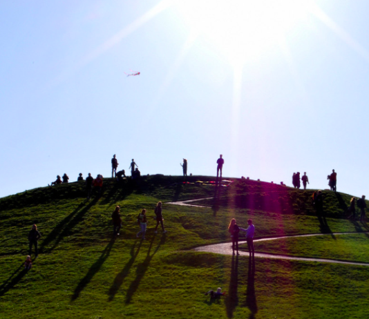 Achieving New Heights: Spring 2022 Publication Update a photo of people standing on a green hill under a blue sky