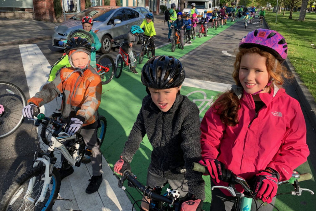 Kids in the Ravenna Blvd bike lane smiling at the camera. The line of kids biking extends very far back