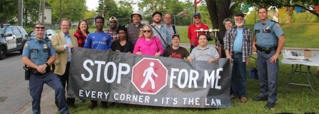 Group of people including police officers holding a Stop for Me Every Corner Its the Law sign