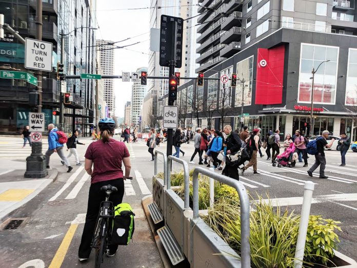 A bike rider waits at a busy intersection in downtown Seattle as pedestrians cross