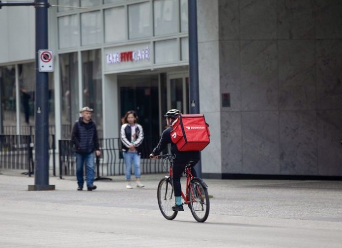 A bicycle delivery worker with a red bag.
