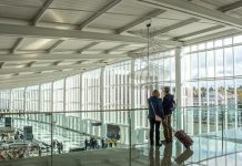 Transpo Notes: Sea-Tac International Arrivals Facility Opens, East Link Delays, Sound Transit Report Dismisses West Seattle Aerial Gondola A photo of two travelers overlooking a baggage terminal in an airport with large glass windows.