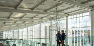 A photo of two travelers overlooking a baggage terminal in an airport with large glass windows.