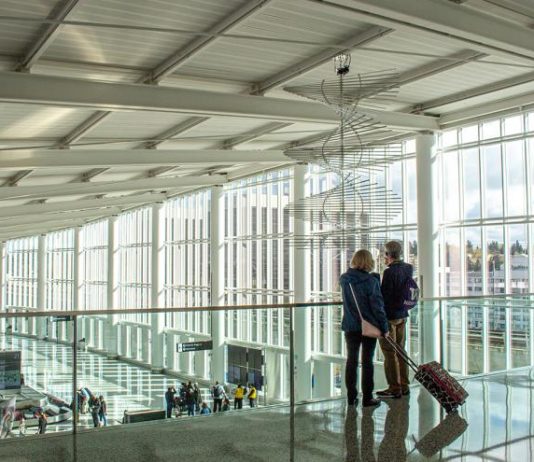 Transpo Notes: Sea-Tac International Arrivals Facility Opens, East Link Delays, Sound Transit Report Dismisses West Seattle Aerial Gondola A photo of two travelers overlooking a baggage terminal in an airport with large glass windows.