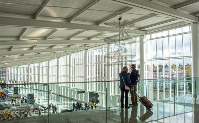A photo of two travelers overlooking a baggage terminal in an airport with large glass windows.