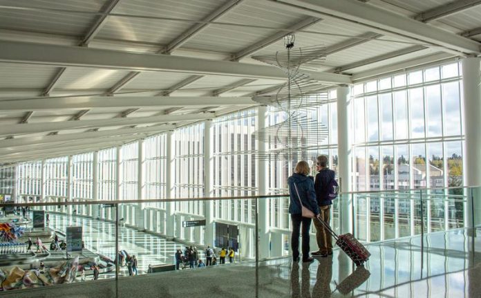 International Arrivals SeaTac A photo of two travelers overlooking a baggage terminal in an airport with large glass windows.