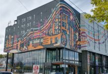 Op-Ed: Opportunity Zones Fail to Address Urban Disinvestment Crisis A gray and white midrise building with an orange art wrap.