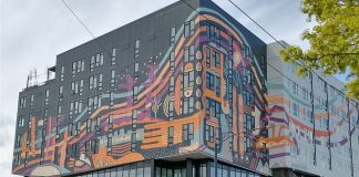 Op-Ed: Opportunity Zones Fail to Address Urban Disinvestment Crisis A gray and white midrise building with an orange art wrap.