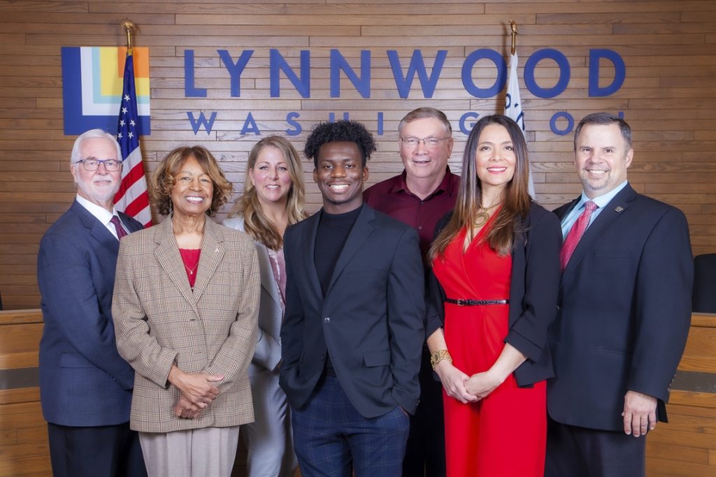 Seven people on the Lynnwood city council in front of a sign saying Lynnwood Washington