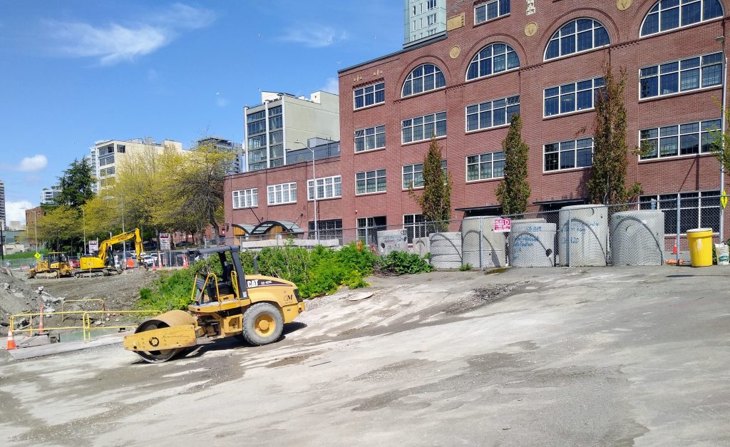 Paved lot next to a four-to-five story building with other residential buildings visible behind it.