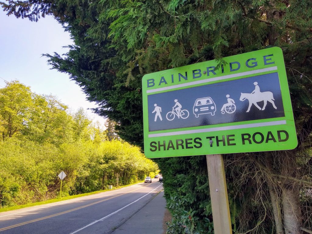 A close op of a sign that read Bainbridge Shares the Road next to a two lane road with paint bike lanes.