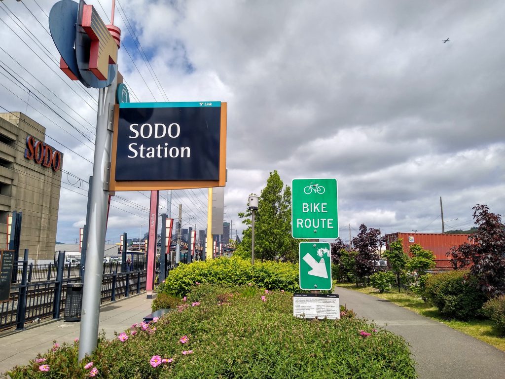 A Sound Transit sign for SoDo station with a bike route sign pointing to the SoDo trail