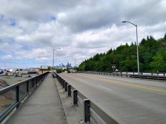 A photo of a narrow sidewalk separated from a roadway by a metal rail.