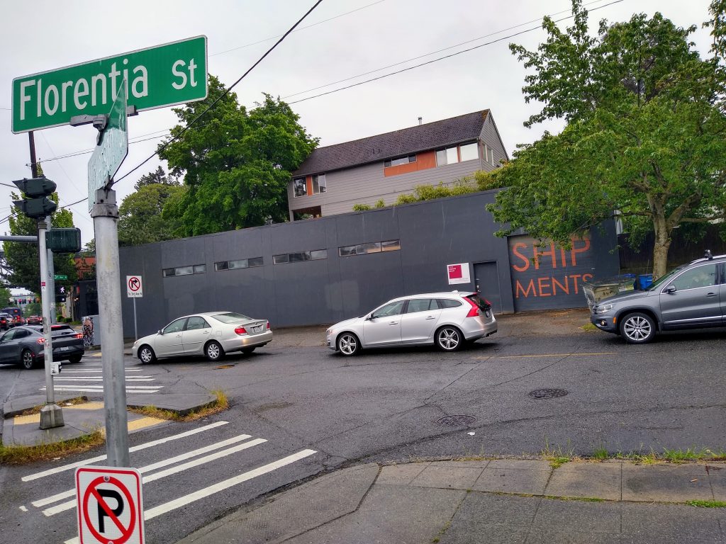 A two lane road with several cars waiting to make a right turn, including one partially blocking the crosswalk