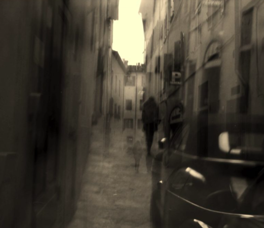 The View From Nathan’s Bus: The Glue That Holds Us Together A blurred black and white photo of a figure walking down a street and a car.