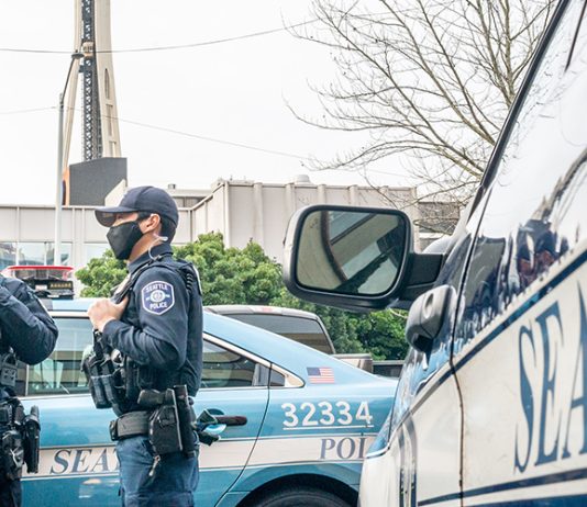 Council Committee Greenlights $1 Million Aimed at Luring More Police Officers to Seattle Three officers standing around a squad car