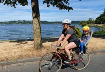 Seattle Calls on Residents to Shape Its Transportation Future a mother bikes with her chair in the rear on a street near a lake