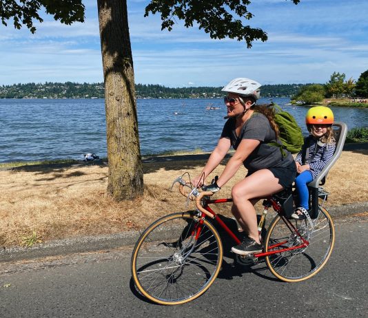 Seattle Calls on Residents to Shape Its Transportation Future a mother bikes with her chair in the rear on a street near a lake