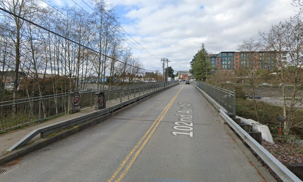 A two lane road with a double center line over a river, with a path separated by a fence on one side