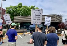 Amazon Walks Away from Warehouse Plans Near Mount Baker Light Rail Station people stand in a parking lot holding stands calling for more community investment