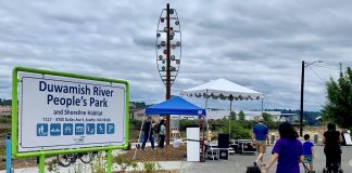 a sign for duwamish people's park with a woman and young child walking by